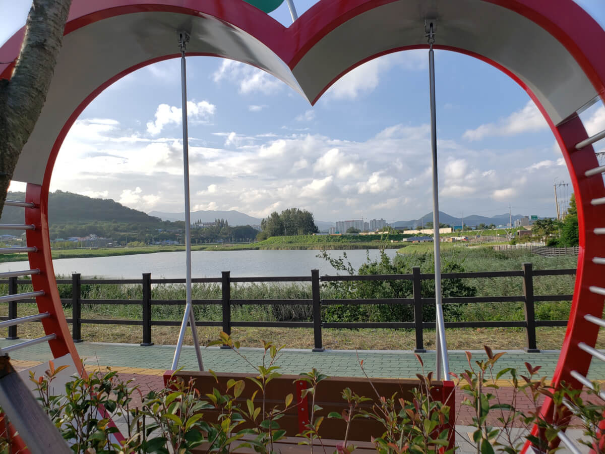 View of sunam reservoir and baegse park through a heart-shaped structure with a bench with mountains in the background