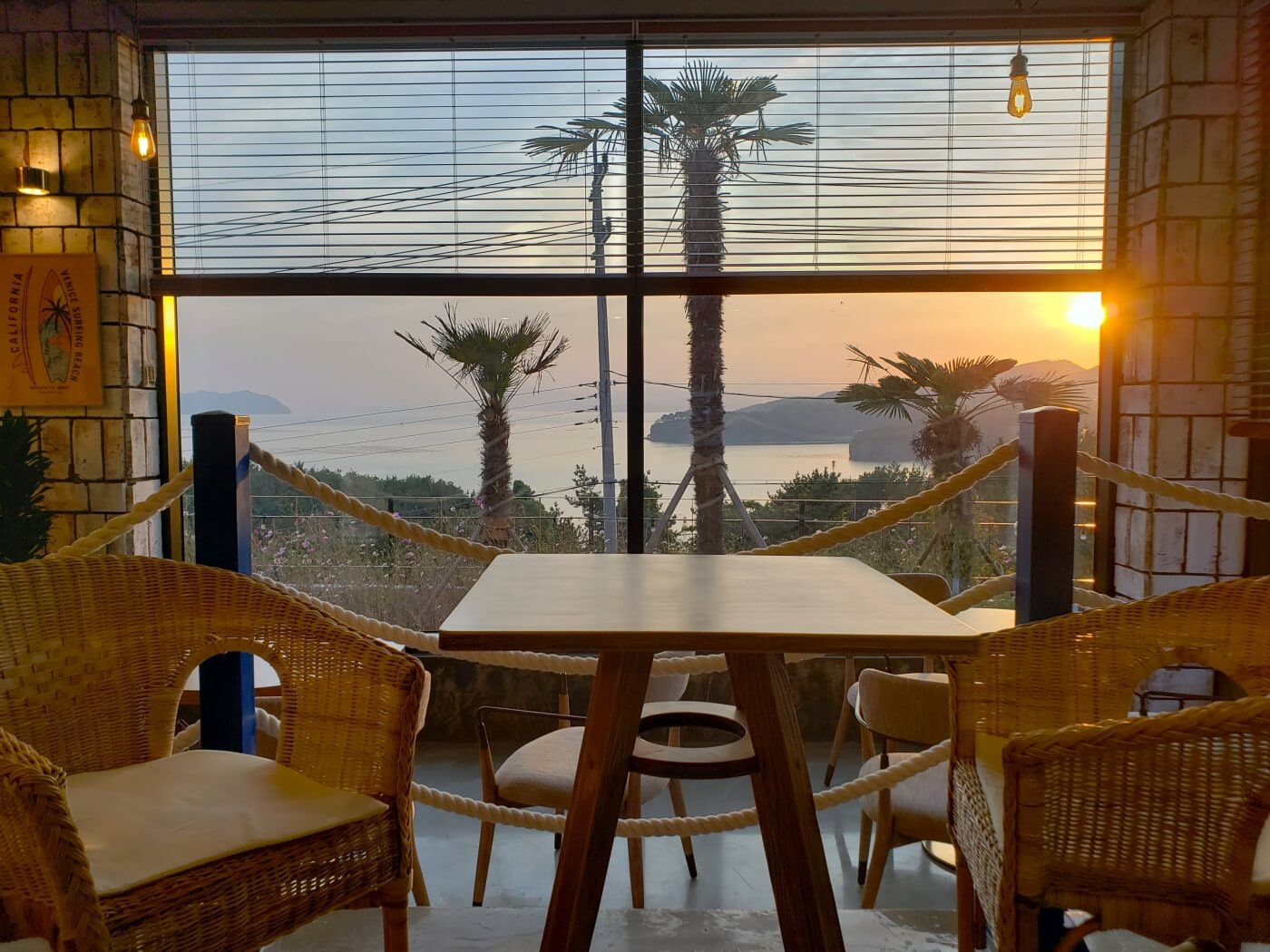 Wicker chairs and a table along a window with a sunset and sea view