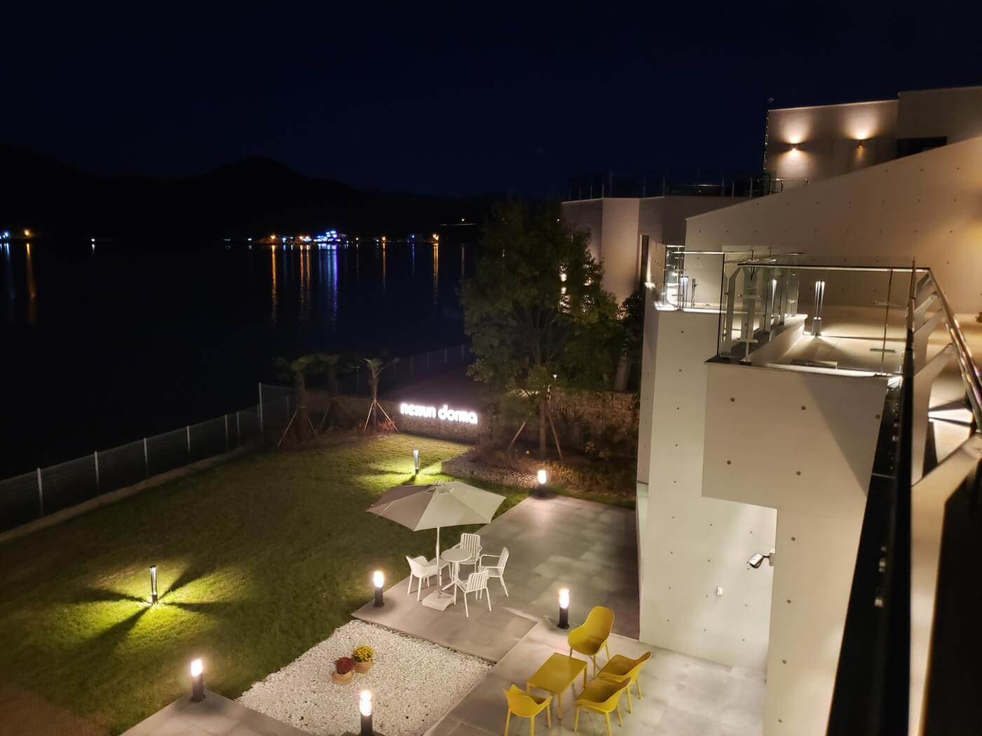 The Nessun Dorma Café yard and patio at night viewed from a balcony with lights on the water
