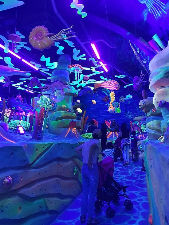 People walking through an underwater scene with glowing colors in the dark in Goseong