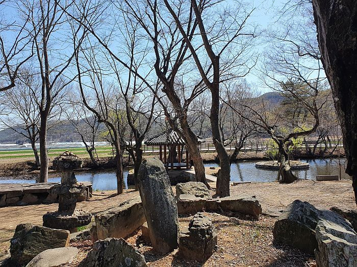 A mound of rocks possibly used as a memorial in front of a pavilion in the center of a pond