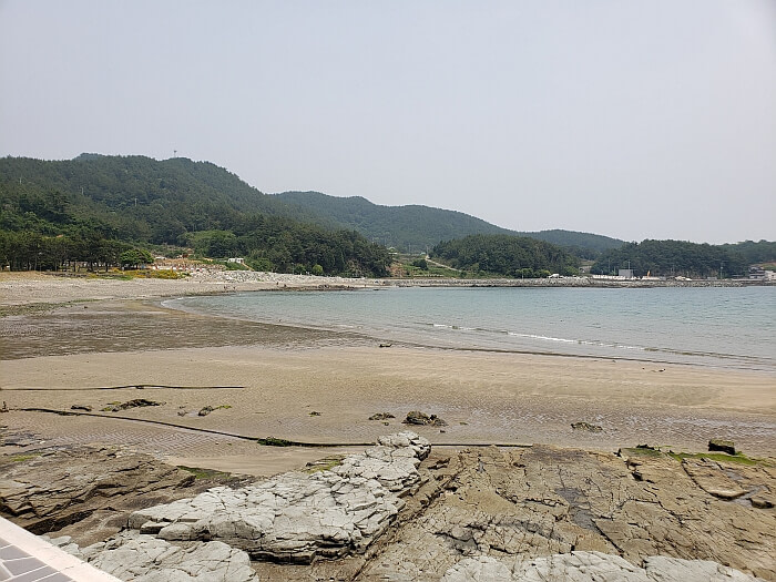 A sandy beach next to some large, flat rocks with mountains in the distance