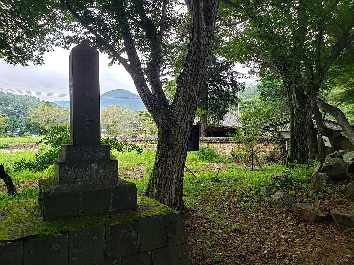 Stone Memorial on a platform at Jangsan Forest next to some trees and the wall of an old hanok village
