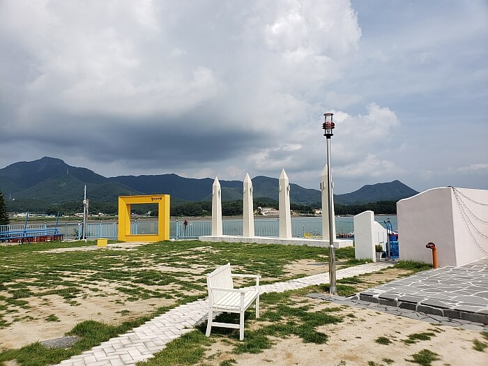 A bench and some pillars with a yellow frame set up outside with clouds hanging over a mountainous background