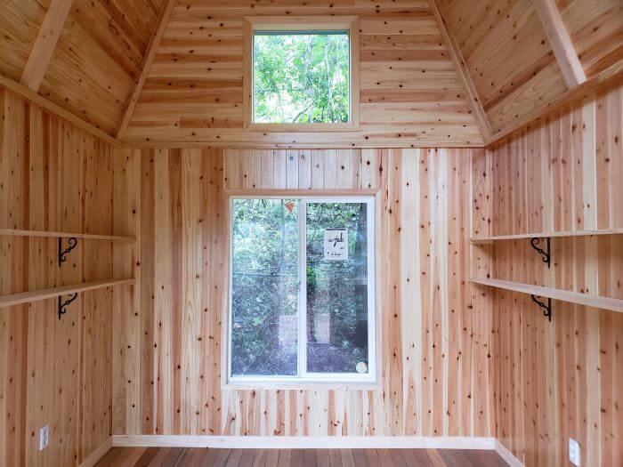 Wooden interior of a small building in the forest with shelves and windows