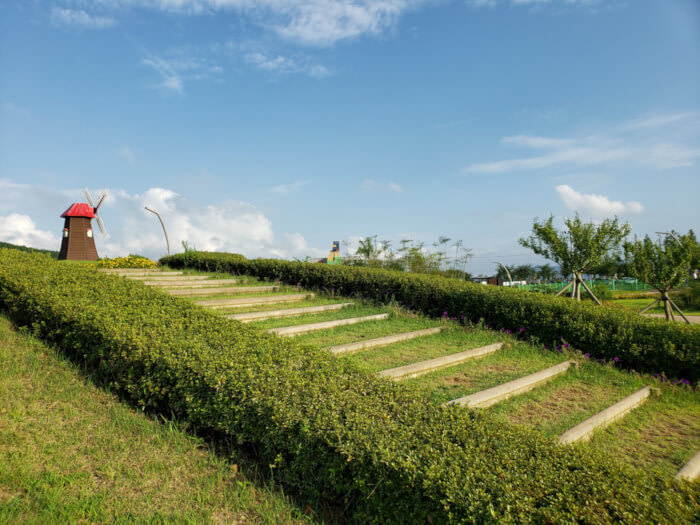 Stairs bordered by bushes leading up to the small hill with the small windmill