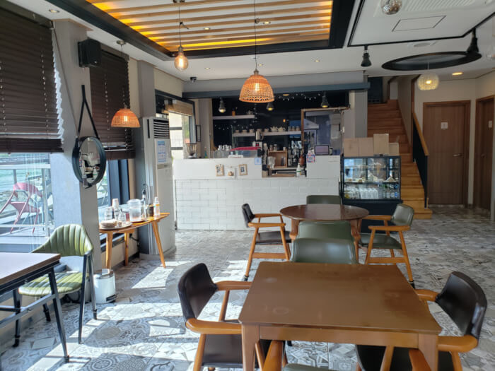 Interior of Sunset Café with several tables and chairs in front of the counter with some dangling lights and sun shining through the window filling the room