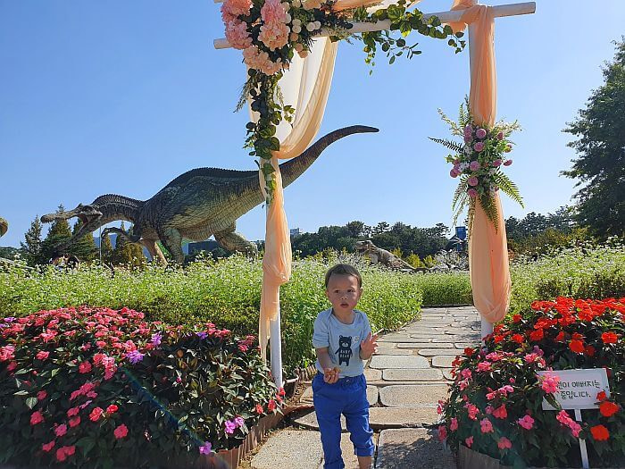 Baby Noah standing under a frame between flowering plants holding dinosaur bread