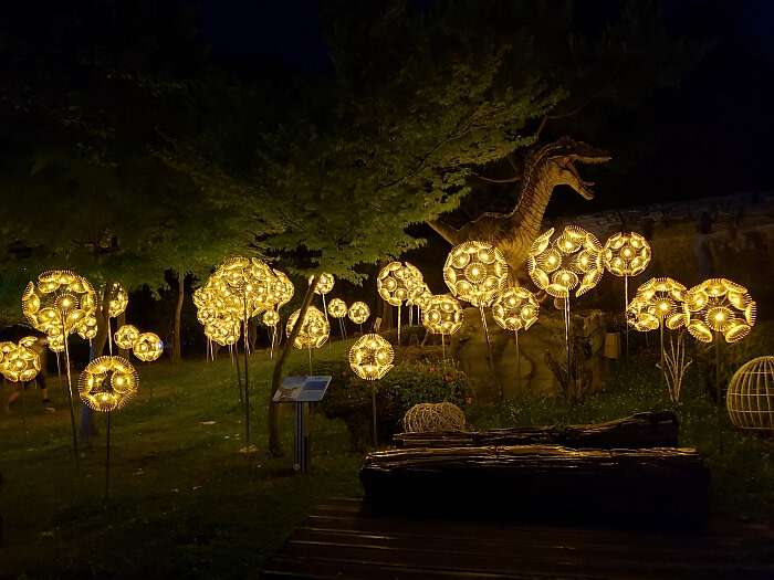 Petrified wood set up among trees and glowing golden orbs with a dinosaur at night