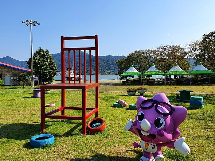 A large, red chair and a purple dinosaur character in a grassy photo zone
