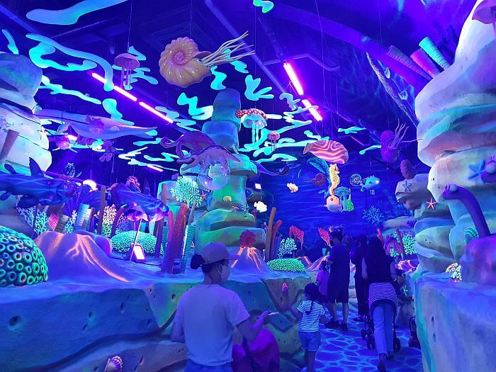 People strolling through an underwater scene in the dinosaur theme park with colors glowing in the dark