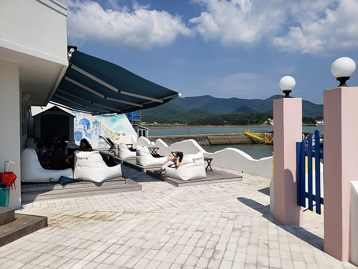 Cushiony chairs near a Greece mural on the wall overlooking the mountains on a very clear day with blue sky