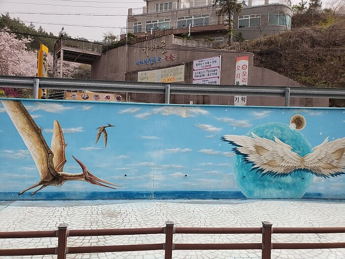 A painted mural of a blue sky with a flying dinosaur and wings