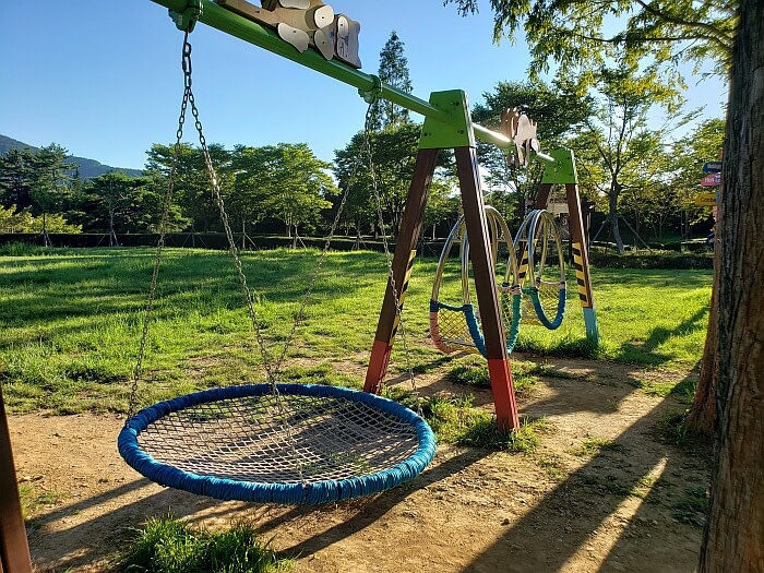 A circular netted swing set in a field near sunset with long shadows
