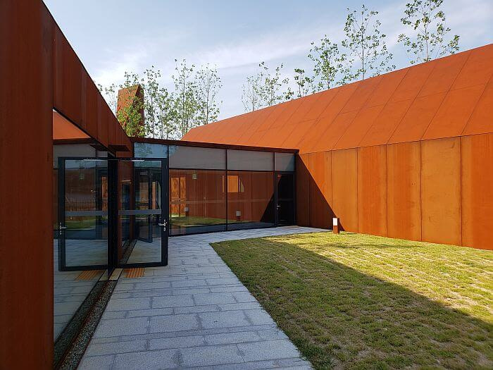 Grassy area between the steel structures with a rusty color and one of them having an open door