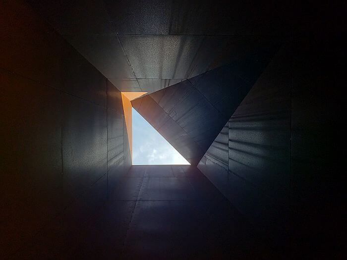 Light shining from blue sky through a triangular opening at the top of a steel plate structure