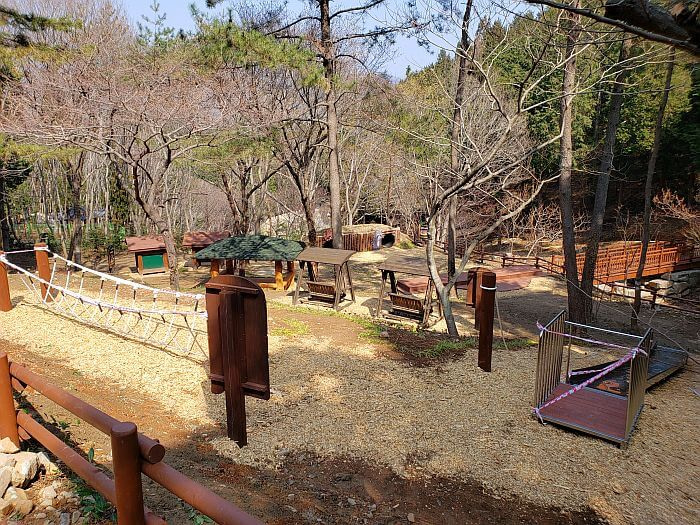 Playground area with a rope bridge, a slide, swinging, benches, etc