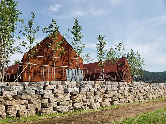 Steel plate structures behind a row of small trees and a railing on a ledge