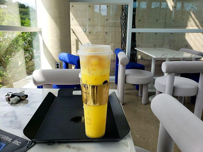 A tall cup of yellow banana drink on a table with cushion chairs