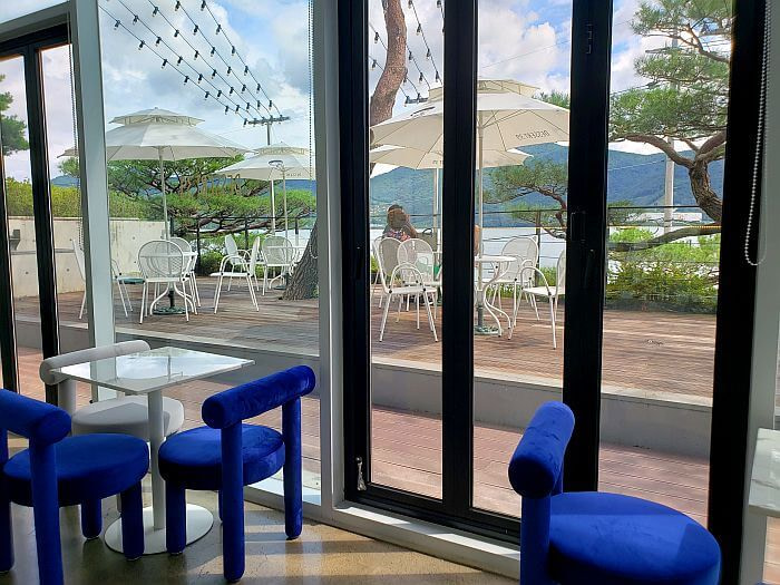 Blue cushion chairs and tables inside along large windows along the outdoor deck
