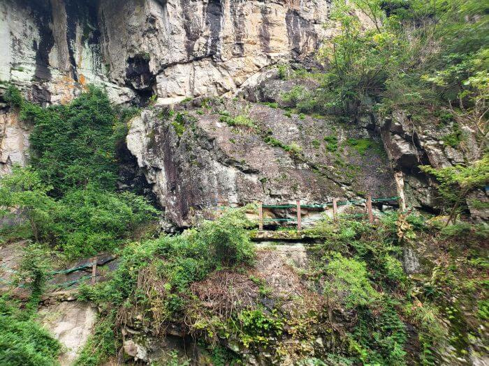 A fence along a path across a rock bridge next to a rocky cliff and waterfall