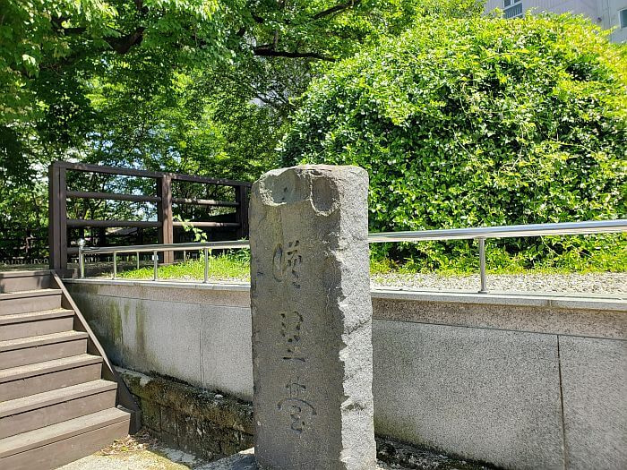 A gravestone next to a burial mound in front of an old tree