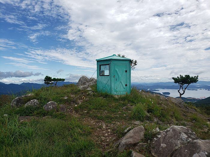 A small, greenish shelter on a mountain peak