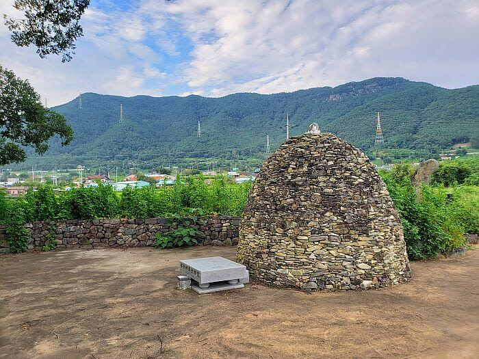 A stone dome near an old tree with a mountainous background