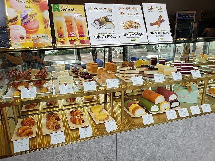 Various bread and dessert menu items on display with pictures and advertisements on top of the display glass
