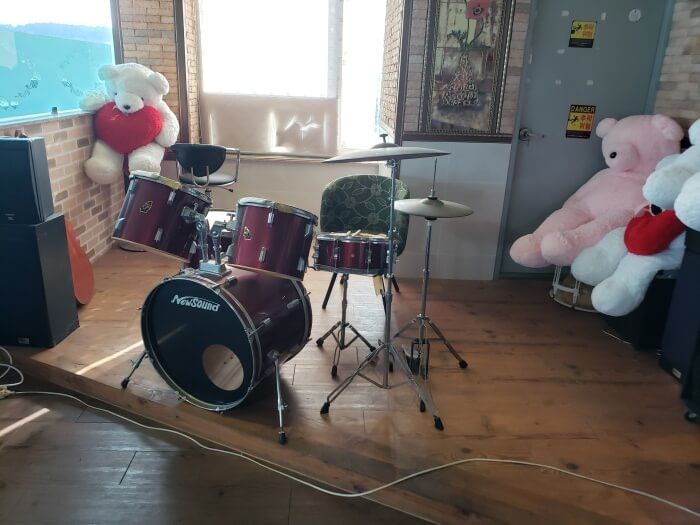 A drumset on a wooden stage next to large teddy bears