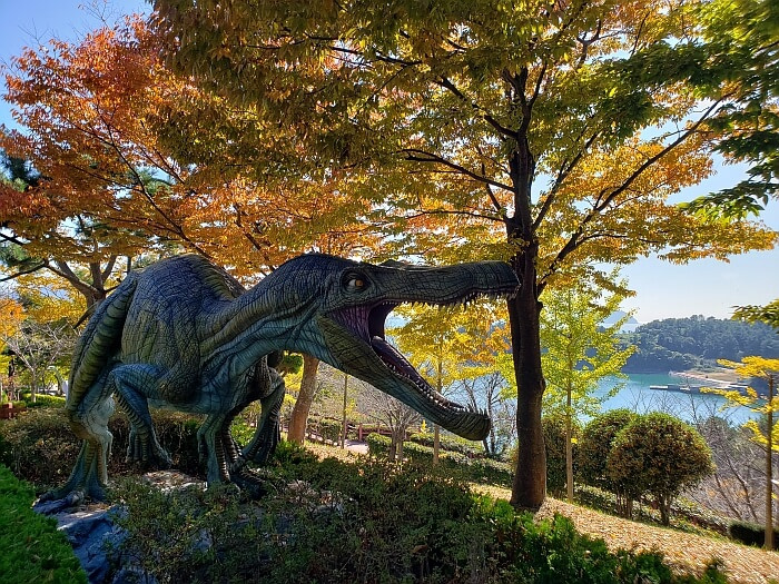 Dinosaur structure with scary-looking, open mouth among colorful trees overlooking the sea