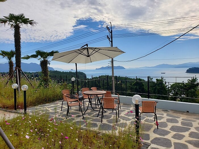Flowers growing around an outdoor patio area with seating and umbrellas with a nice coastal view of the sea