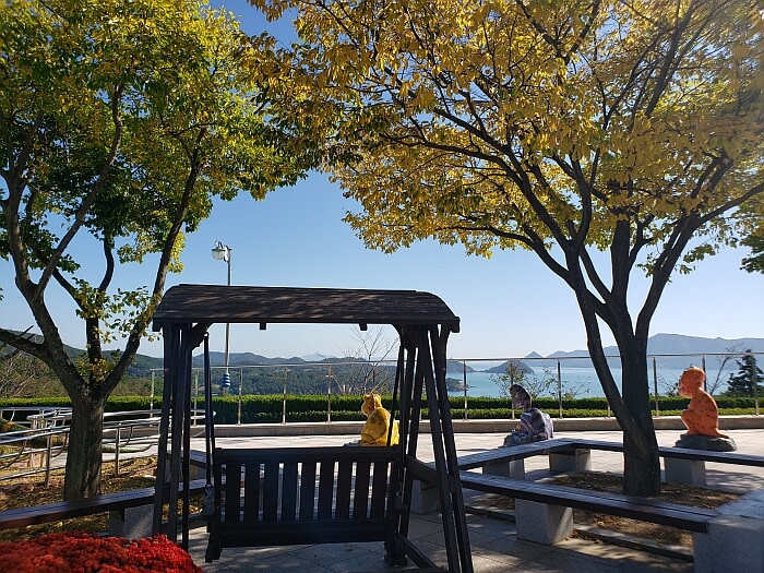A swinging wooden bench under colorful autumn trees with a nice view of the sea