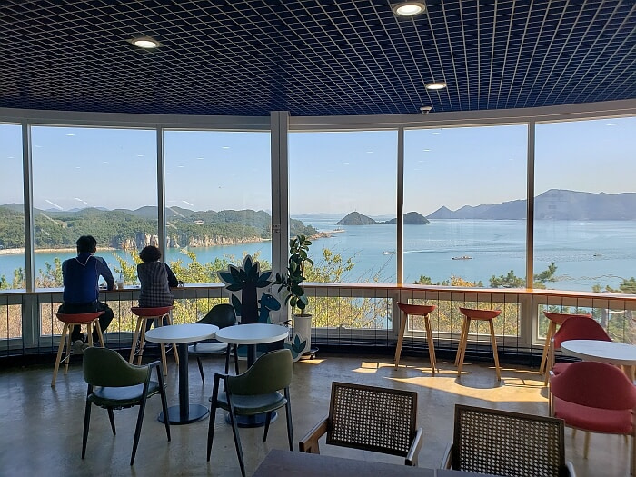 Two people sitting looking out a large window at the sea and islands an observatory café