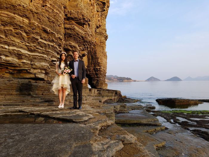 Nate and Alice's wedding photo at Sangjogam Park next to the cliffs and the sea behind them