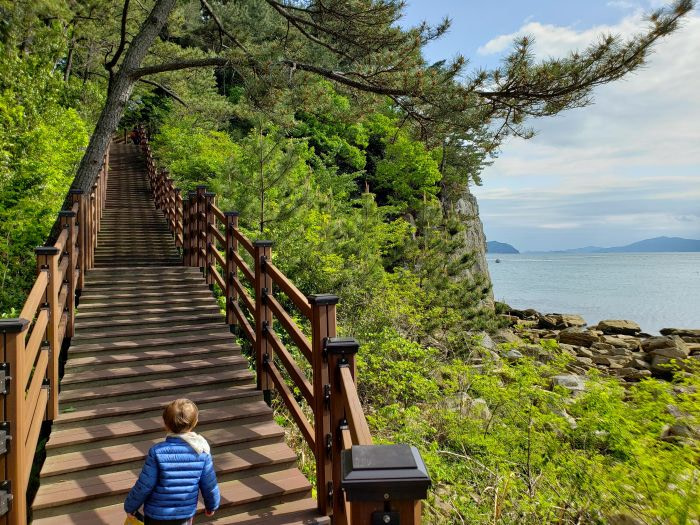 A toddler at the foot of steps of a coastal boardwalk