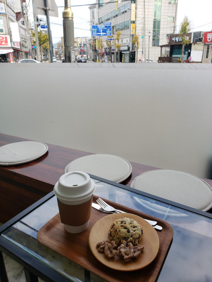 A tray of coffee and a scone on a table next to the window viewing the street