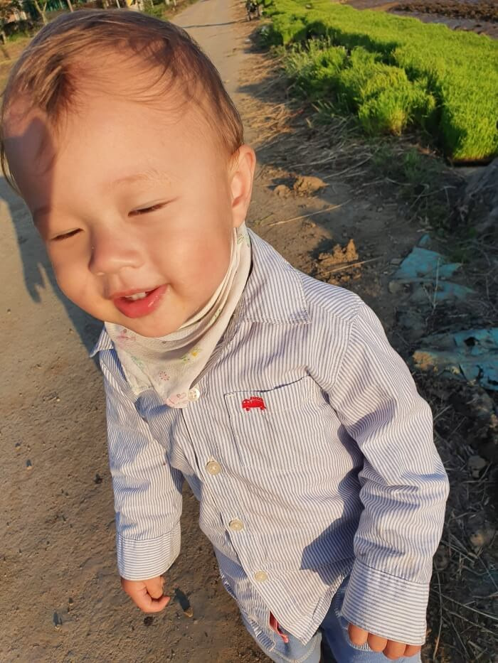 Noah standing and smiling near the edge of the rice field with the sun shining on his face