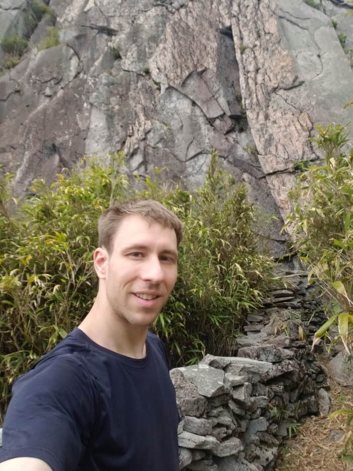 Nate along a wall of stacked rocks and bamboo against a cliff