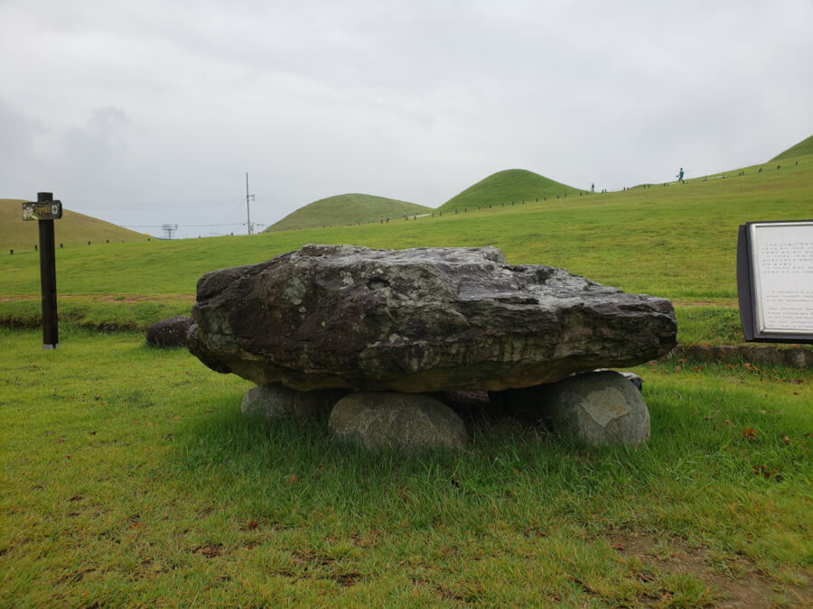Prehistoric rock tomb on the grass with the large cluster of Songhakdong tombs in the background on a cloudy day