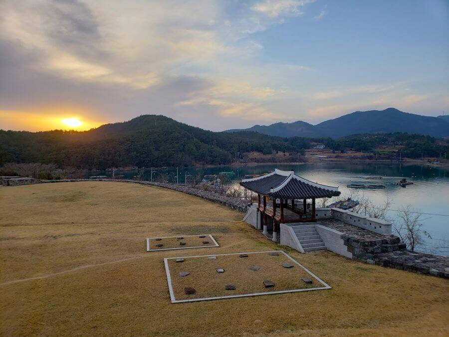 A Korean fortress along water and mountains at sunset