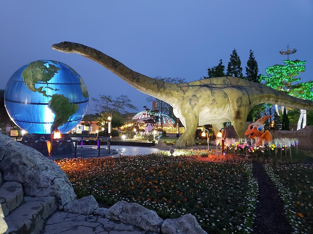 A large dinosaur in the Dinosaur Theme Park in Goseong with a long neck sticking its head over a large globe