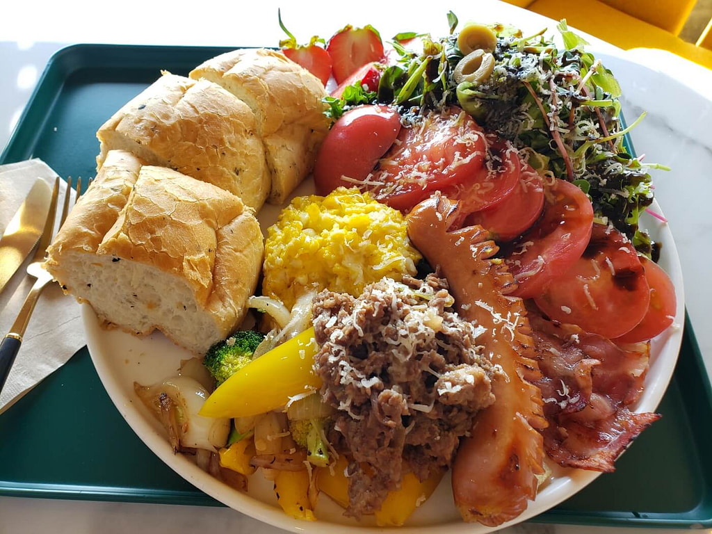 A brunch plate at The Wave Café with sausage, bacon, egg, salad, bread, etc