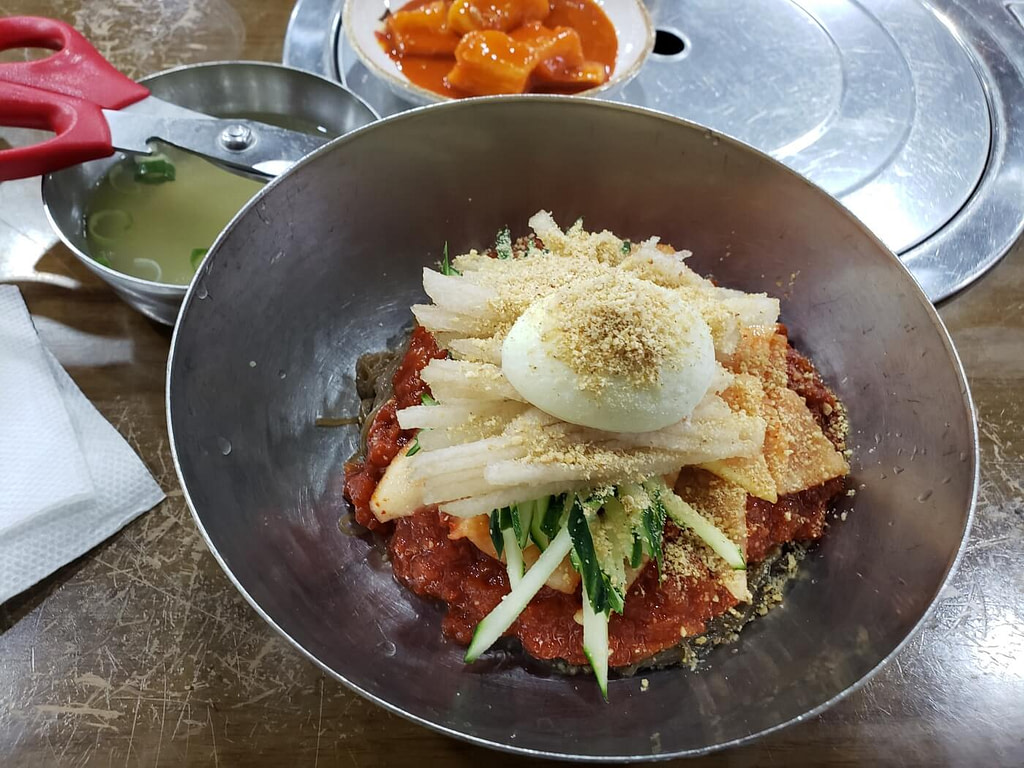A bowl of Korean bibim naengmyeon topped with shredded veggies and a boiled egg