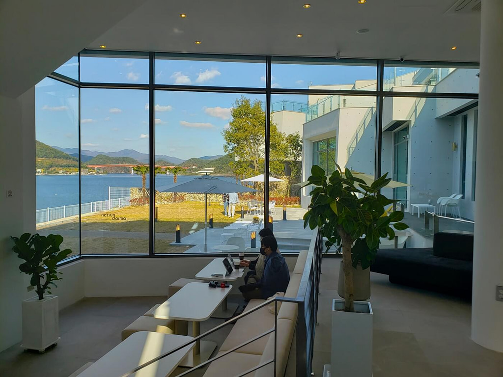People sitting on cushion seats next to large windows with a view of an orange bridge over the water