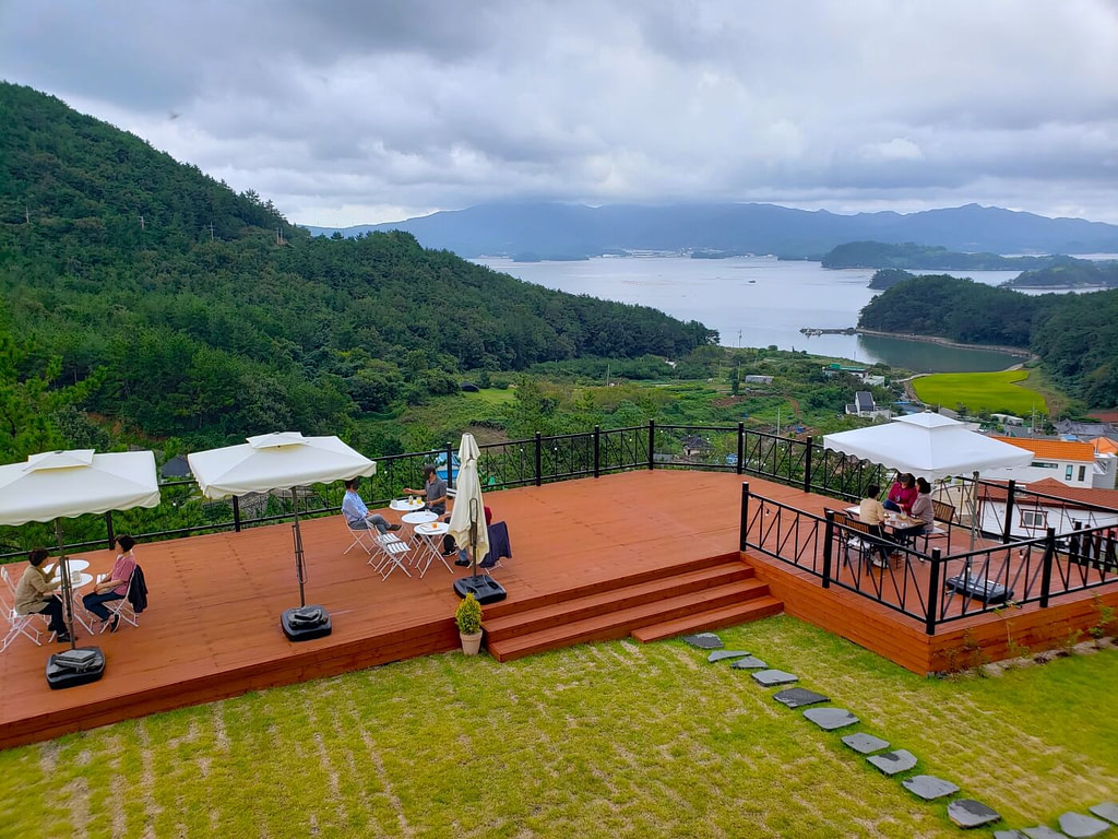 People sitting at tables covered by umbrellas on an outdoor patio overlooking a view of the sea and mountains