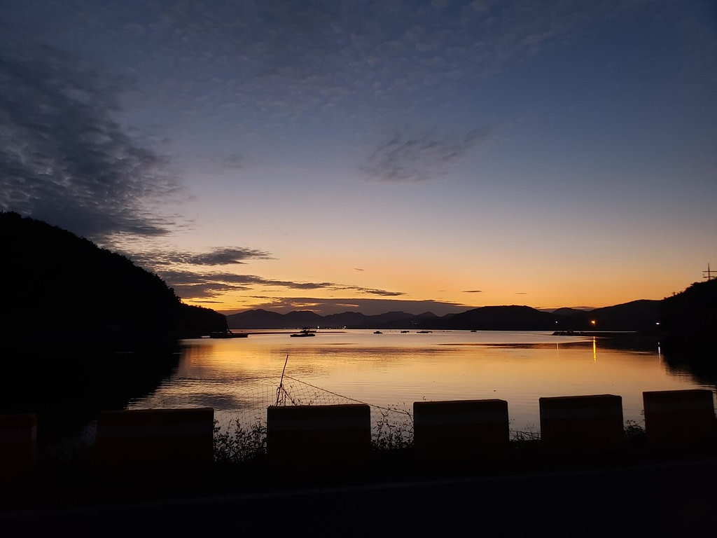A sunset over calm water along the side of a country road in Goseong, South Korea