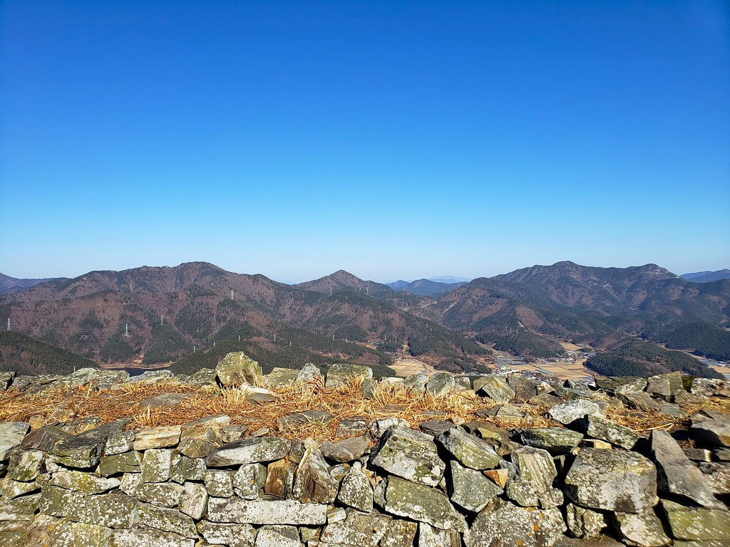 A rock wall with mountains in the distance and villages at the base