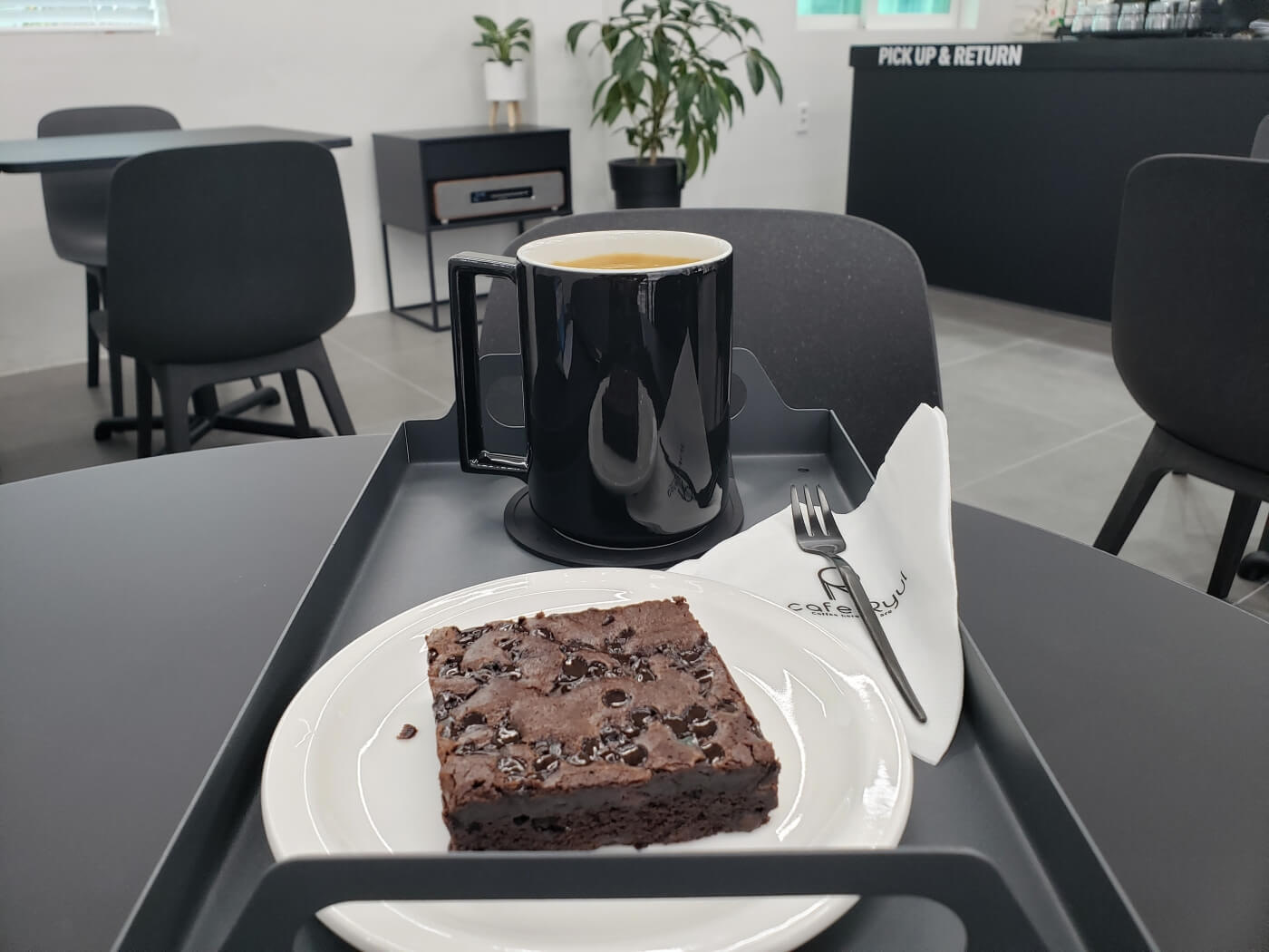 A chocolate brownie and a mug of coffee on a tray on a table