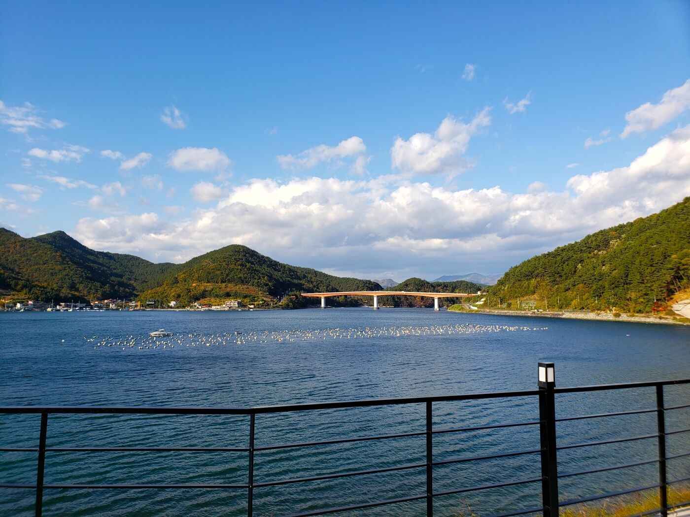 An orange bridge over calm water with white clouds and blue sky